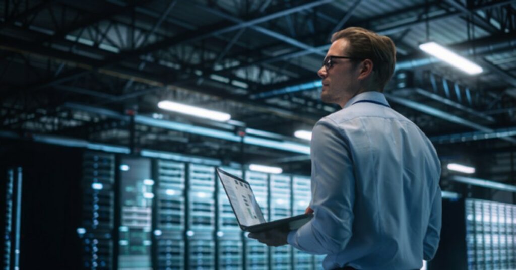man standing in a server room with a laptop